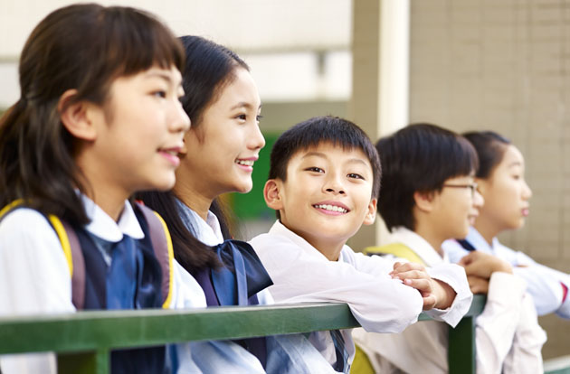 Chinese children in school uniforms smiling and leaning against rail