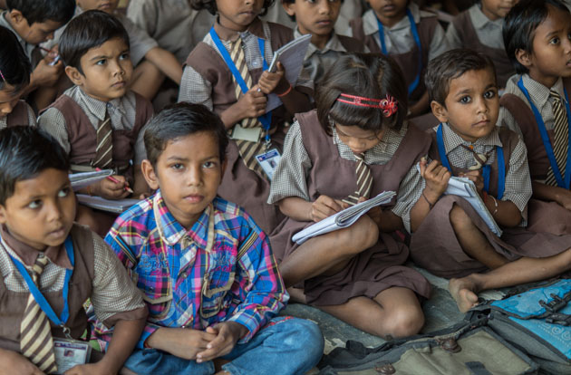 South Asian children in school uniform sit on floor and write notes