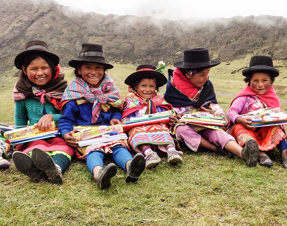 Peruvian girls wearing hats sitting in a valley holding their school supplies in their laps