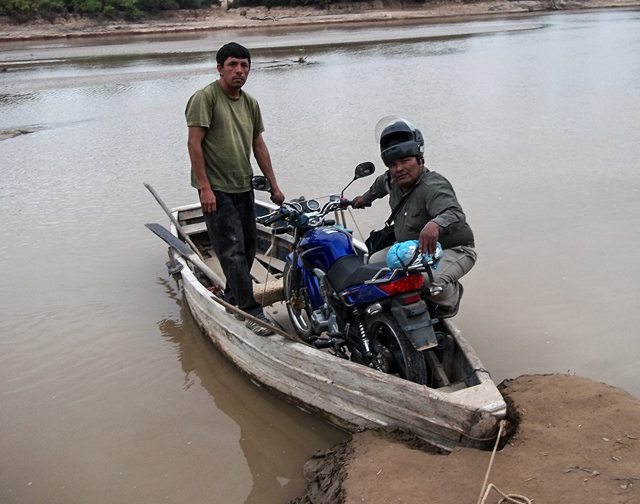 Two Argentinian men in a small wooden boat transporting a small motorcycle on a river