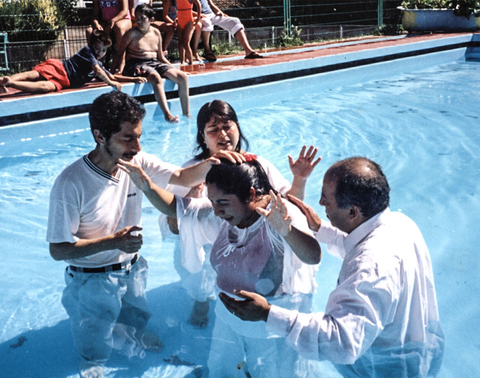 Chilean woman standing in a pool with her hands up after being baptized by two men and a woman