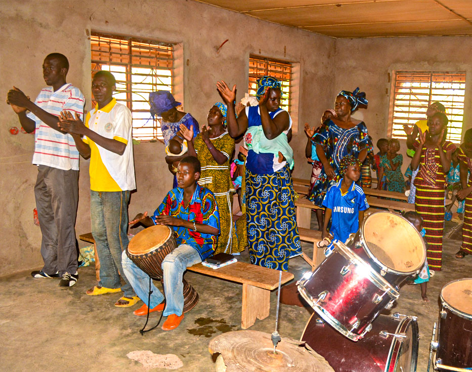 Burkinabé Christians stand in their church clapping their hands, playing drums, and singing praises to God