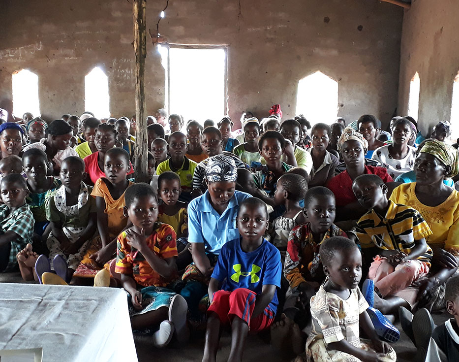 Malawian women and children sitting on the floor together tightly packed in a small building