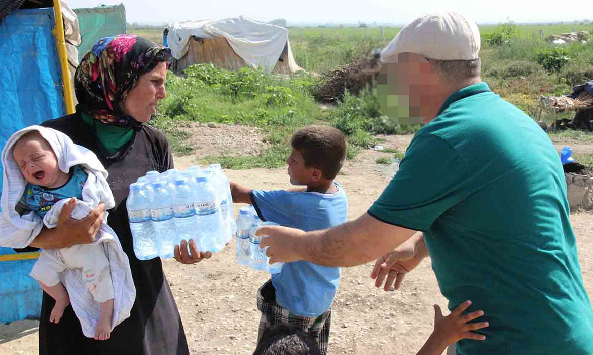 Christian missionary gives package of water bottles to Middle Eastern woman holding her baby
