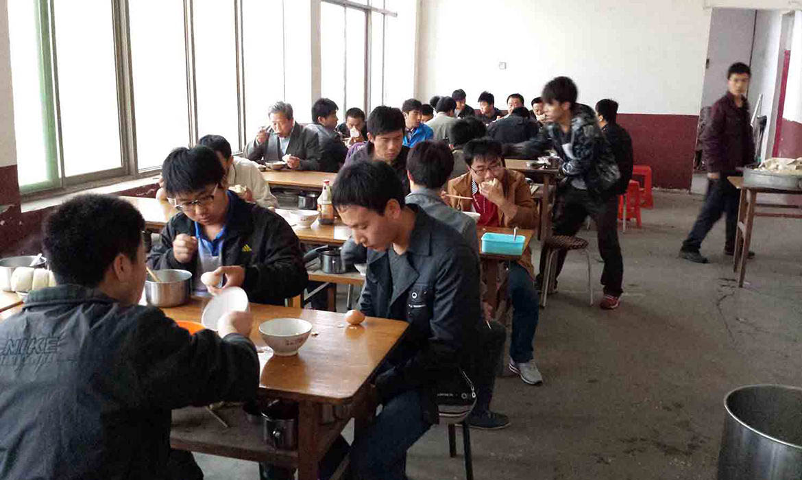 Chinese men sit at rows of wooden tables eating together