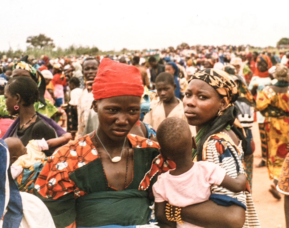 Two Nigerien women one of them holding her baby with lots of other people surrounding them in a crowd