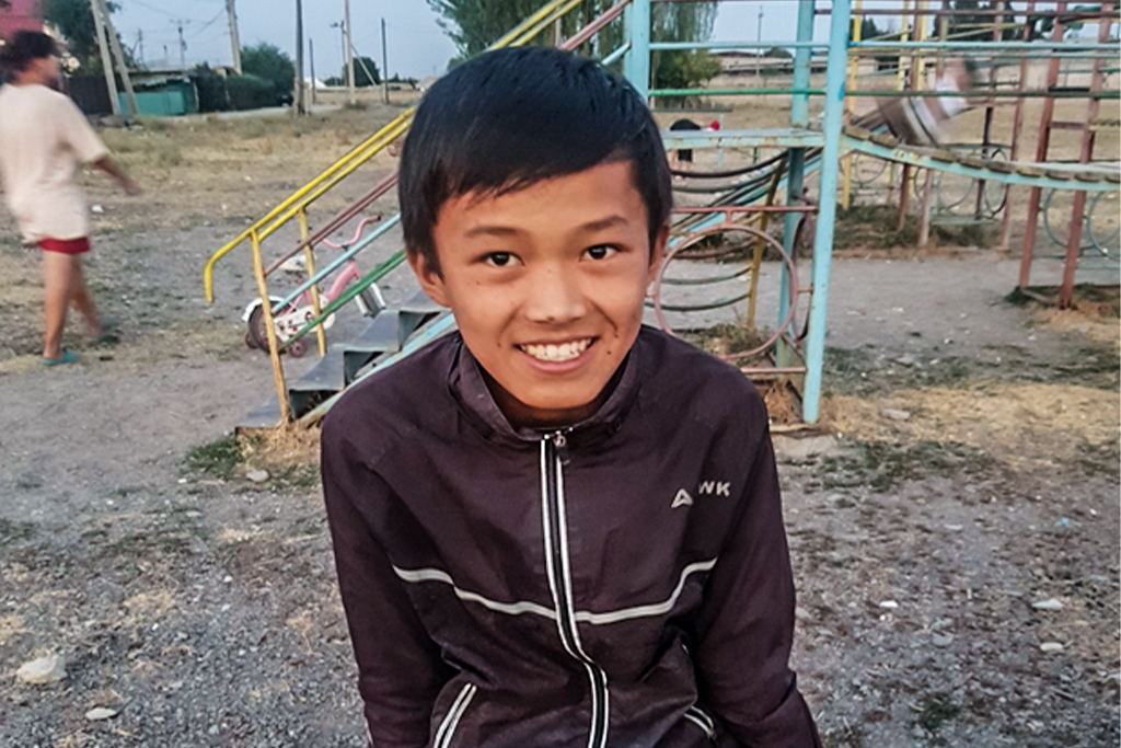Kyrgyz boy smiling while standing in front of a rundown playground
