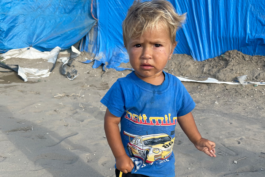 Little boy stands in a camp for Middle Eastern refugees.