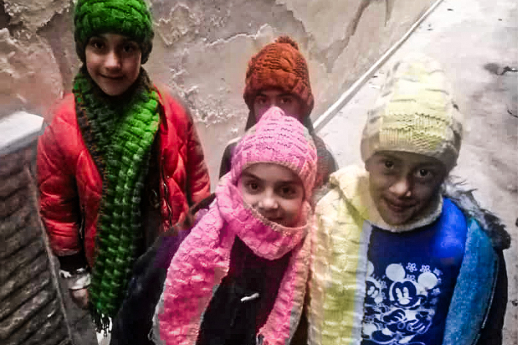 Four Lebanese children dressed in winter coats, hats, and scarves