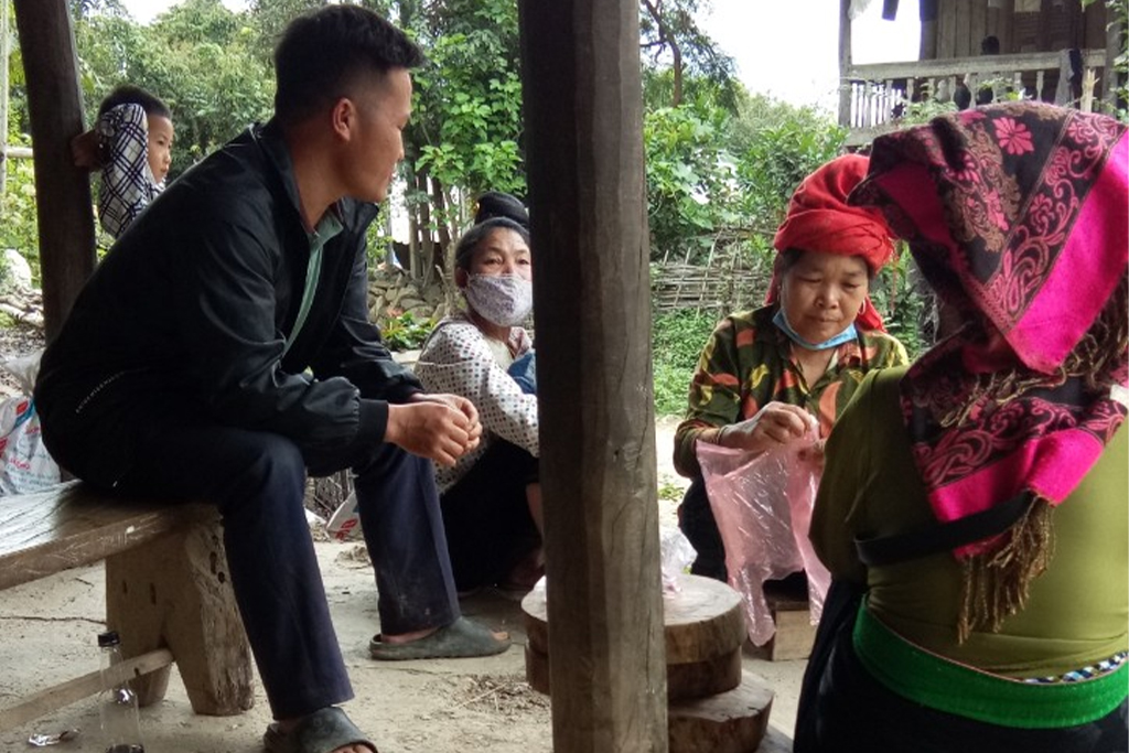 Vietnamese man sitting on a bench under a pavilion while women from his family sit talking to him
