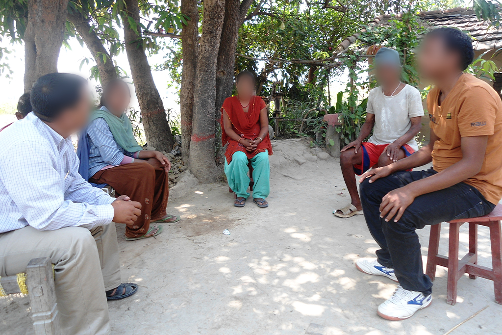 South Asian Christians sitting outside on benches and stools under shady trees