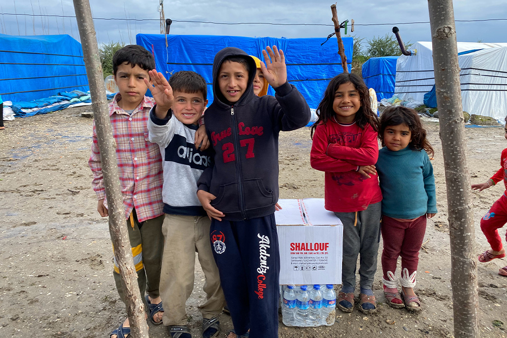Turkish children smiling while standing in a camp that has buildings made from tarps