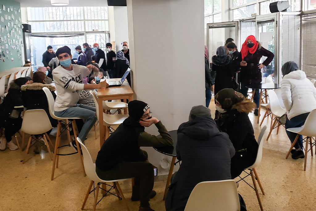 Refugees from the Middle East standing in line and sitting at tables in a refugee center in Europe