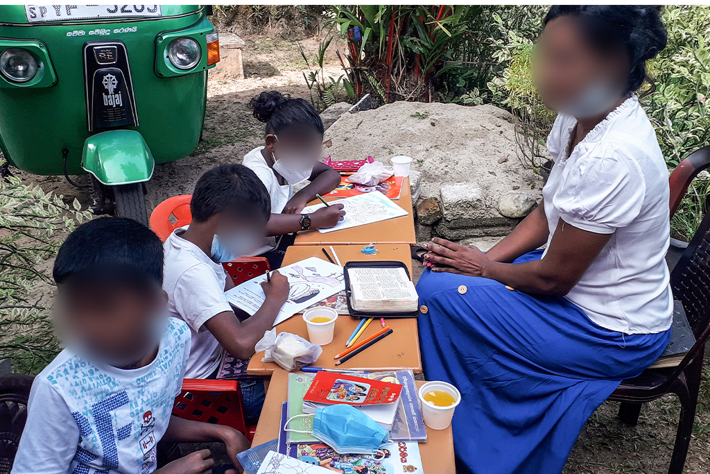 Sri Lankan Christian woman teaches three children from the Bible while they color a Bible story coloring sheet