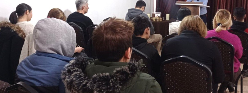 Middle Eastern Christians sitting in rows of chairs in a small building listening to their pastor preach