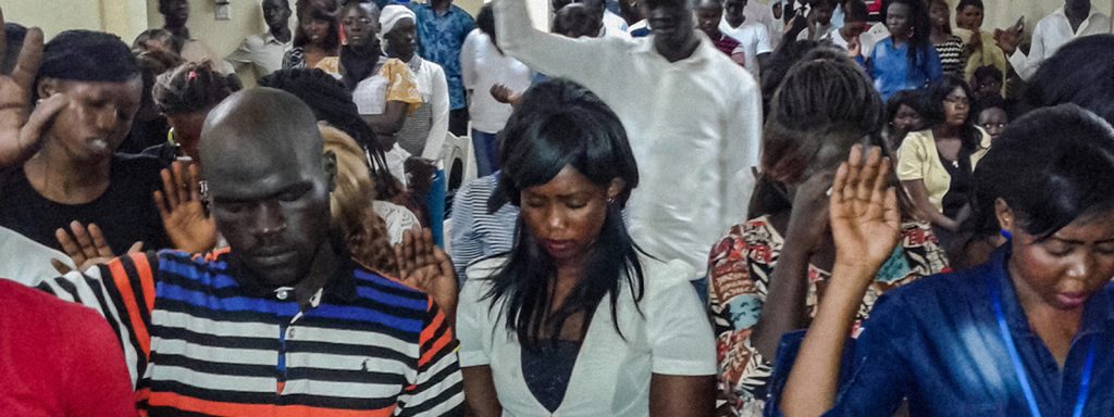 North African Christians sitting and standing in rows with their heads bowed and hands up worshiping God