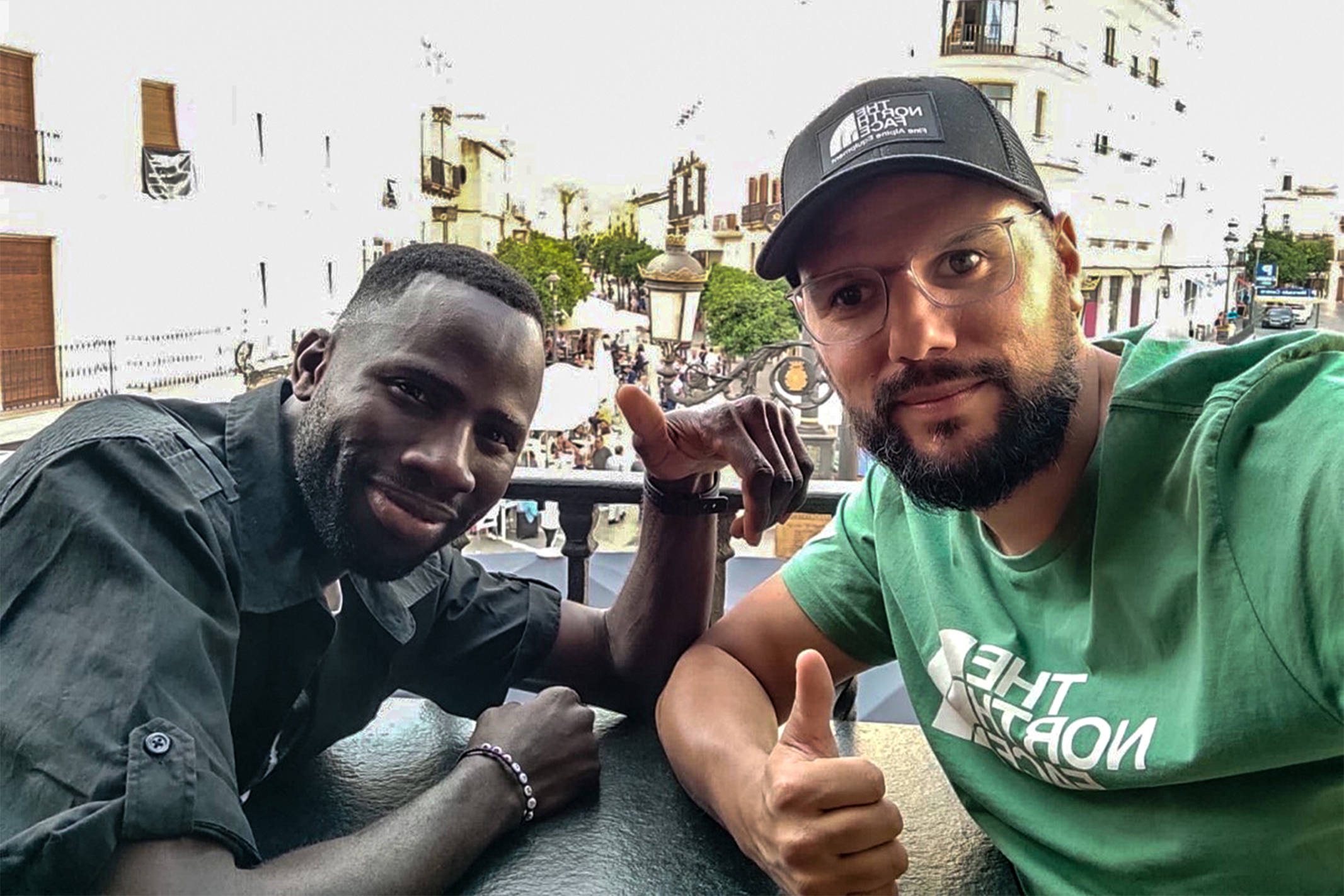 Spanish man in a green North Face shirt taking a selfie with an African man wearing a black shirt