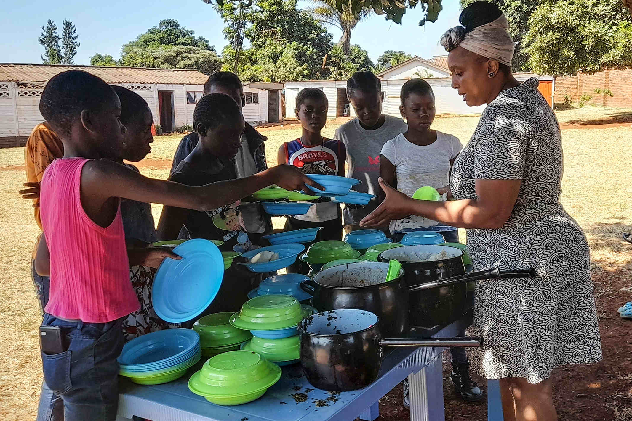 Christian woman in Zimbabwe feeding several children who are holding green and blue bowls