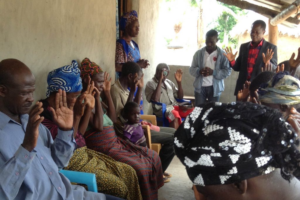 Togolese Christians sit outside on a concrete patio with their hands held up worshiping God