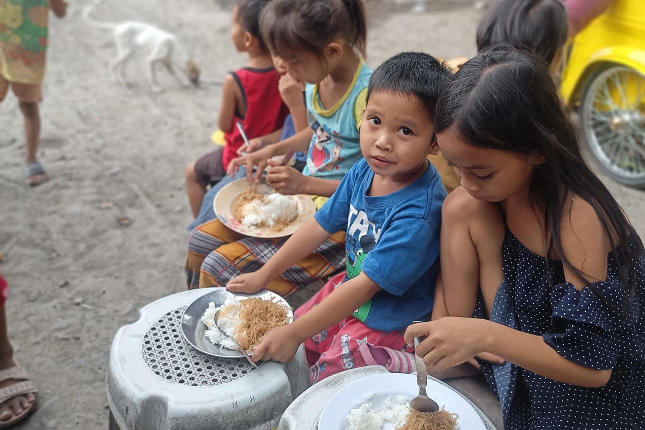 Children in the Philippines sitting outside eating rice and noodles