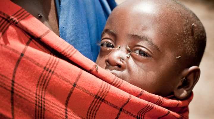 African boy resting in a sling around his mother's shoulder with flies flying around his face