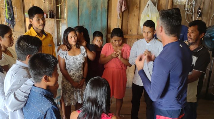 Brazilian Christian missionary prays with men and women in wooden house