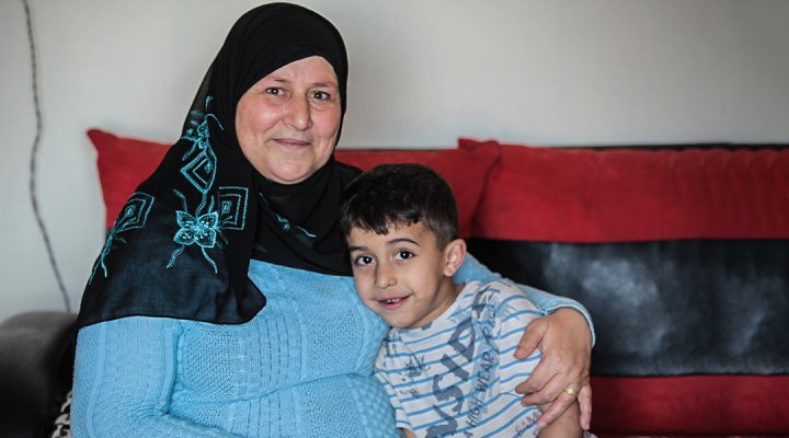 Syrian mother wearing a head covering who is a refugee with her arm around her son
