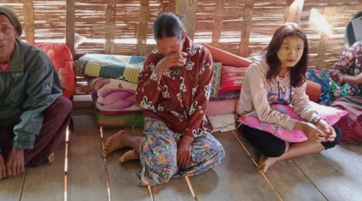 A Burmese family sitting on a wooden floor with blankets behind them