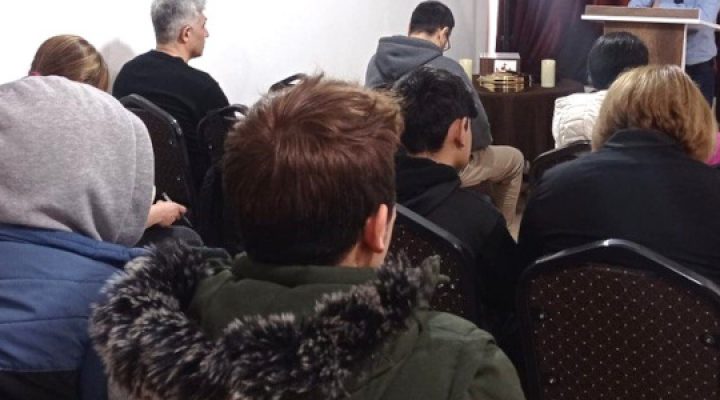 Middle Eastern Christians sitting in rows of chairs in a small building listening to their pastor preach